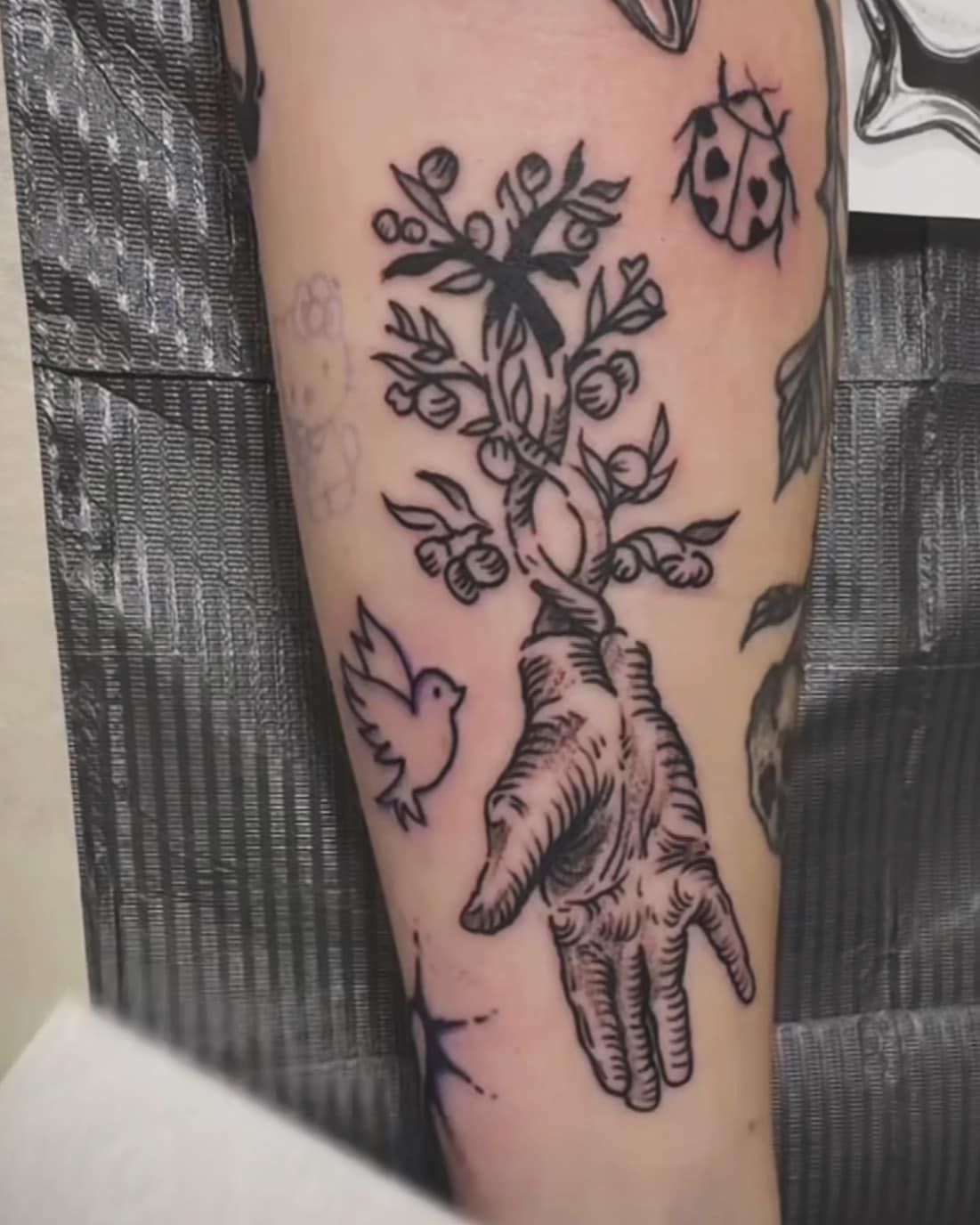 Black-and-gray tattoo on a leg showing a hand with flowers and birds around it.