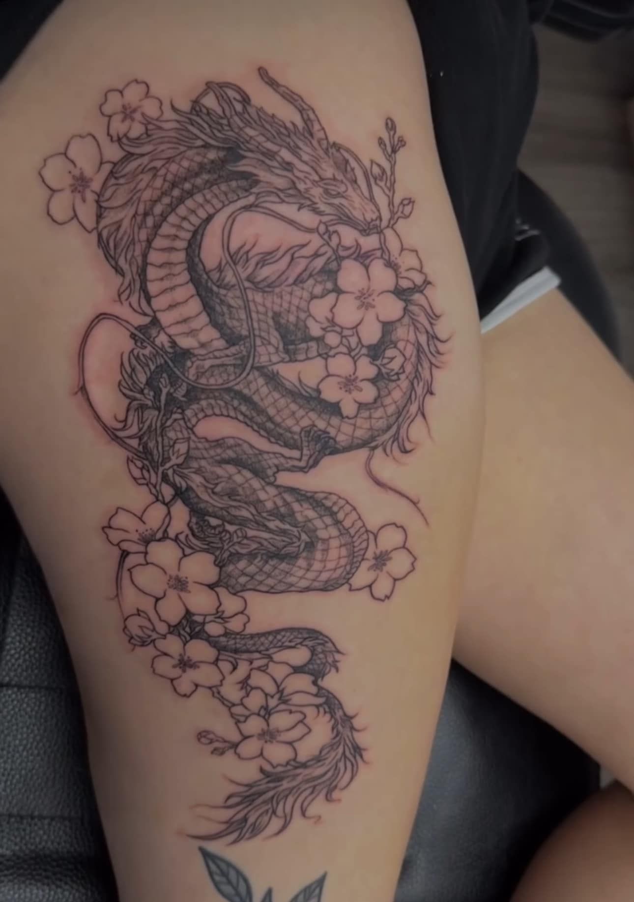 Black-and-white tattoo of a koi fish with cherry blossoms on a thigh