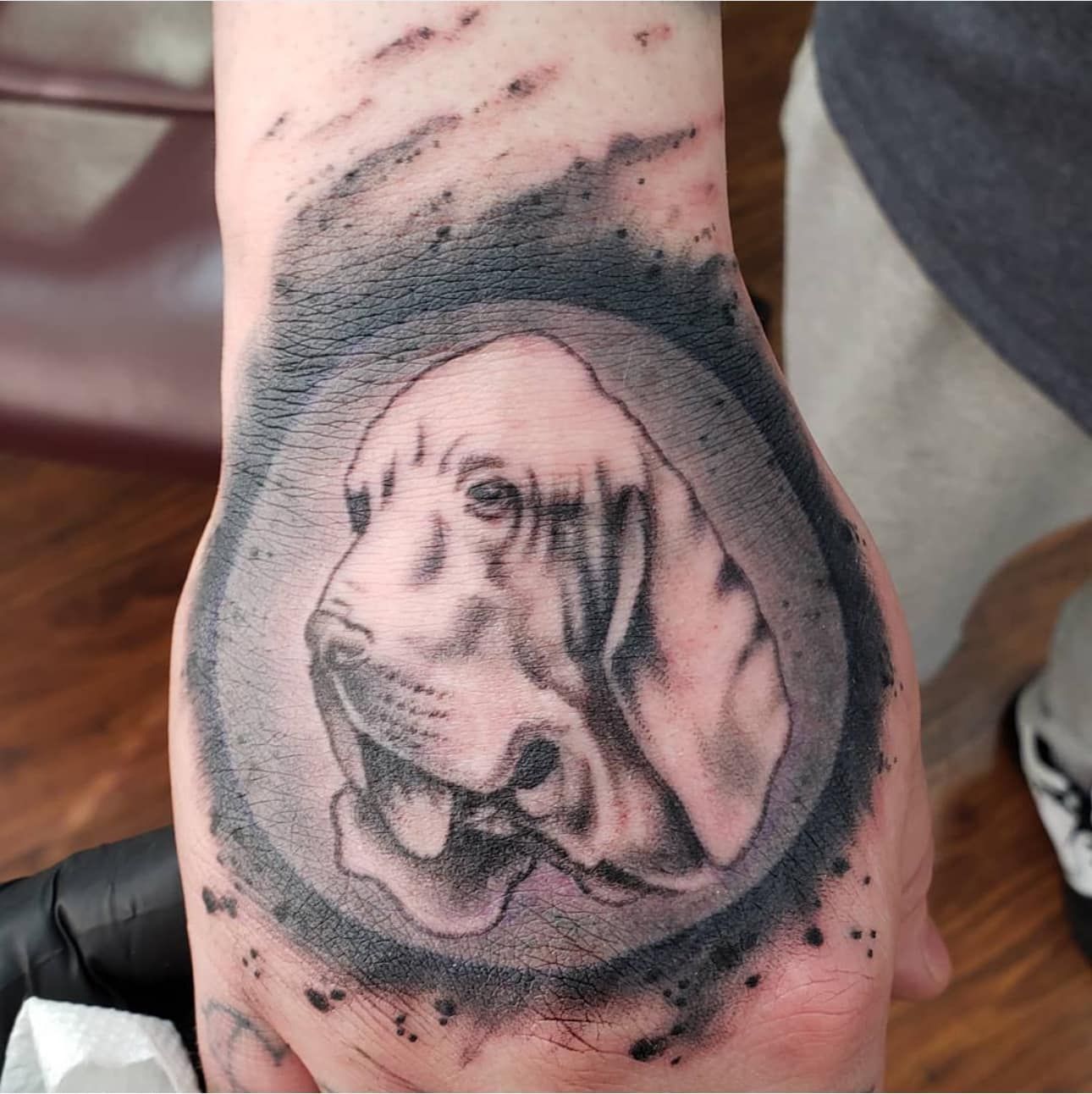 Black and gray dog portrait tattoo on a forearm, with a shaded circular background