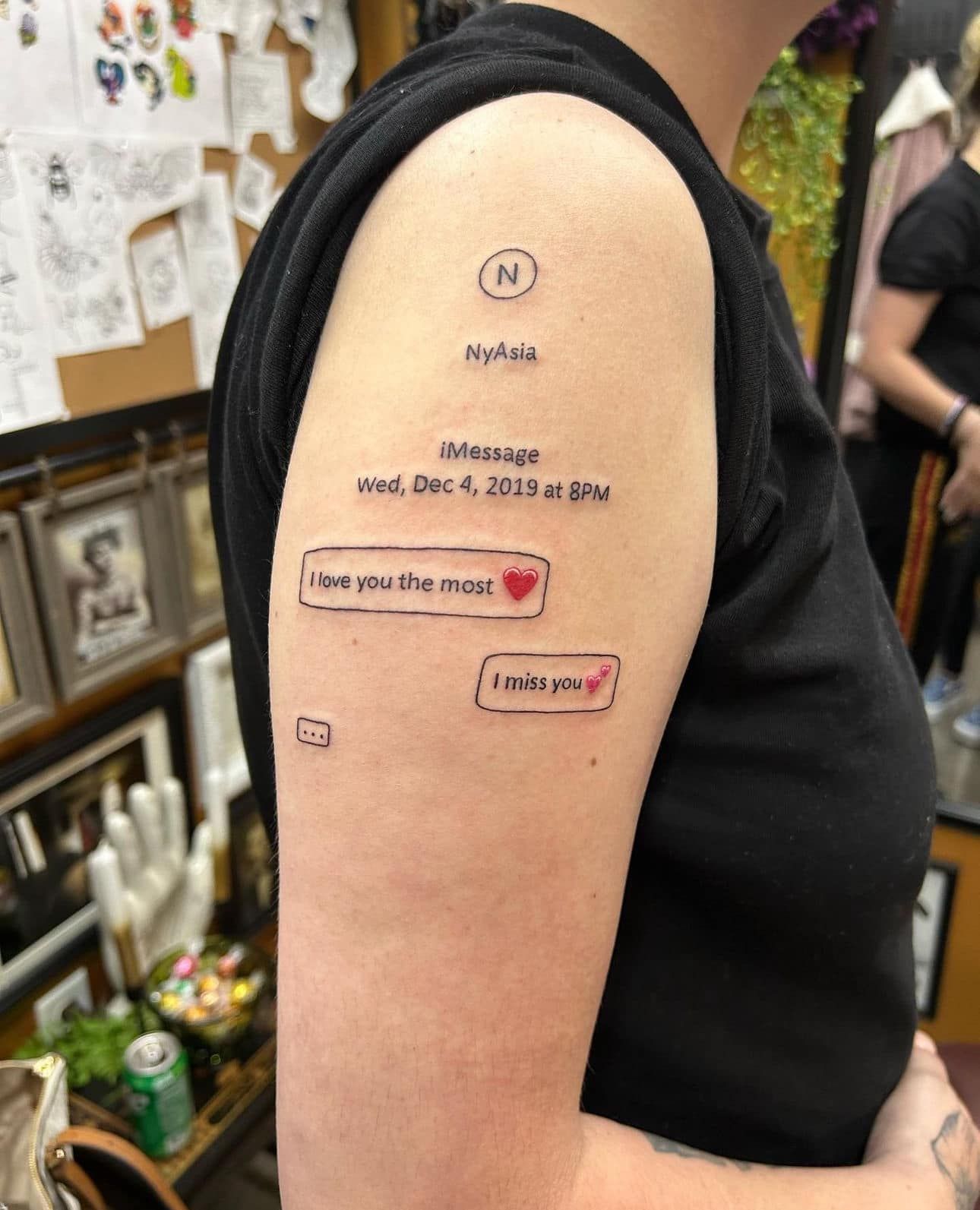 Arm tattoo with small text, a heart, and a red border on a person’s upper arm.