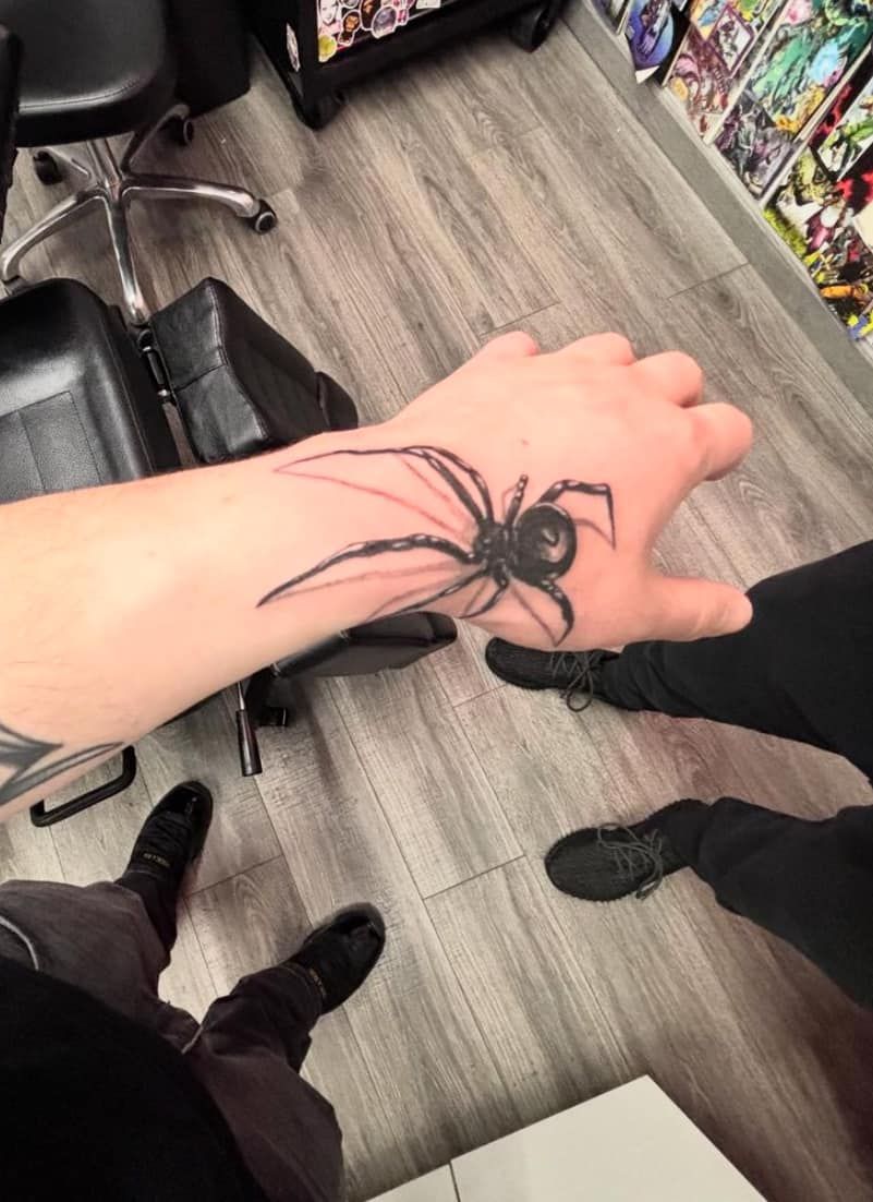 Arm with a large black spider tattoo in a store aisle, viewed from above.
