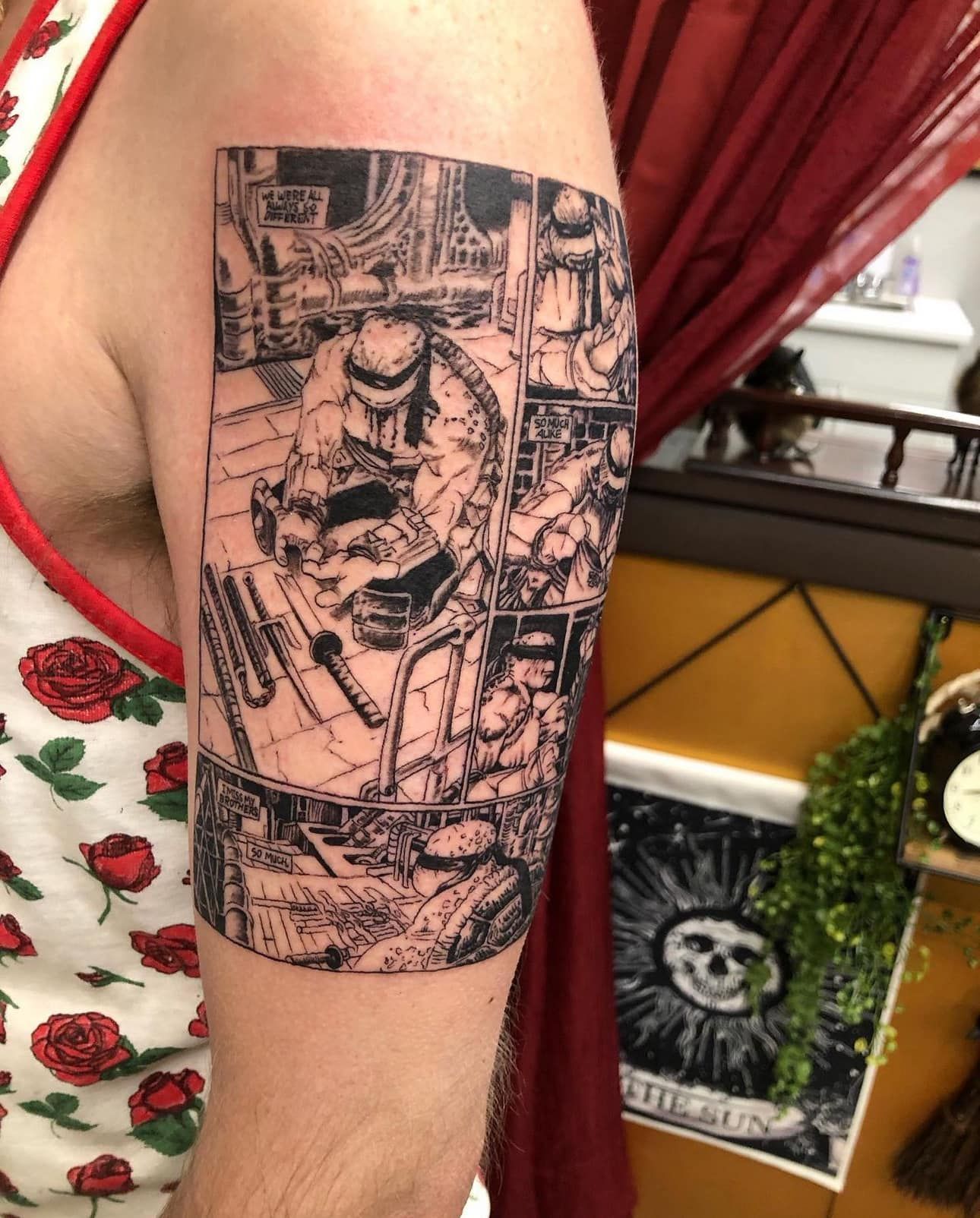 Arm tattoo with a detailed black line-art city scene and figures on a person's upper arm