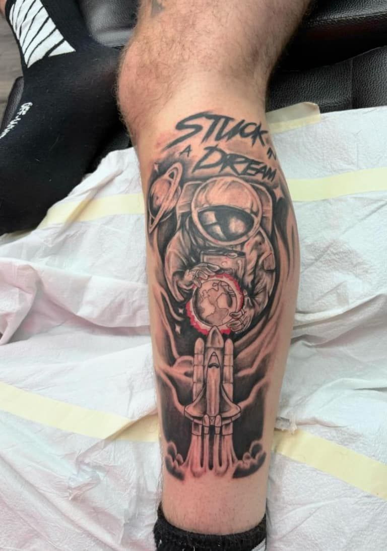 Forearm tattoo of a skull with a large eye and gun, black and gray with red accents