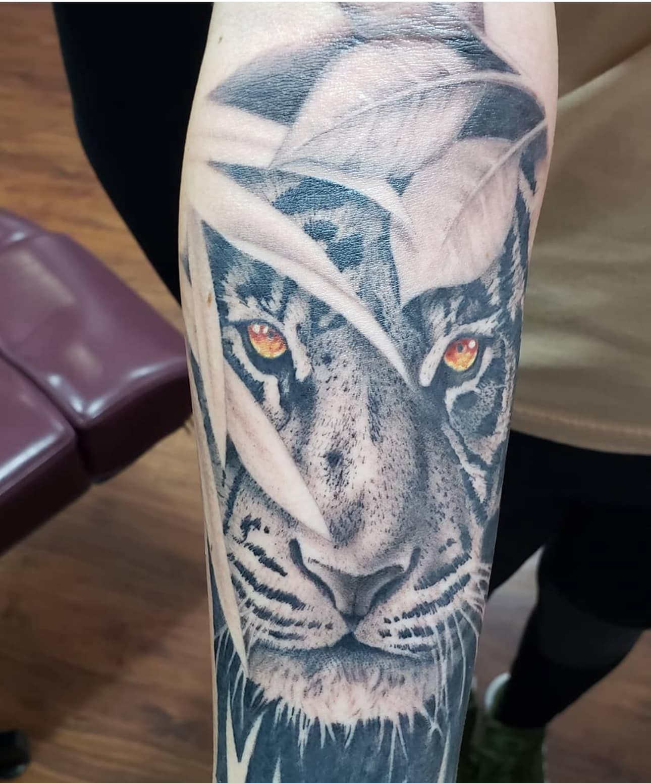 Black-and-white tiger tattoo on a person’s forearm with amber eyes and open mouth