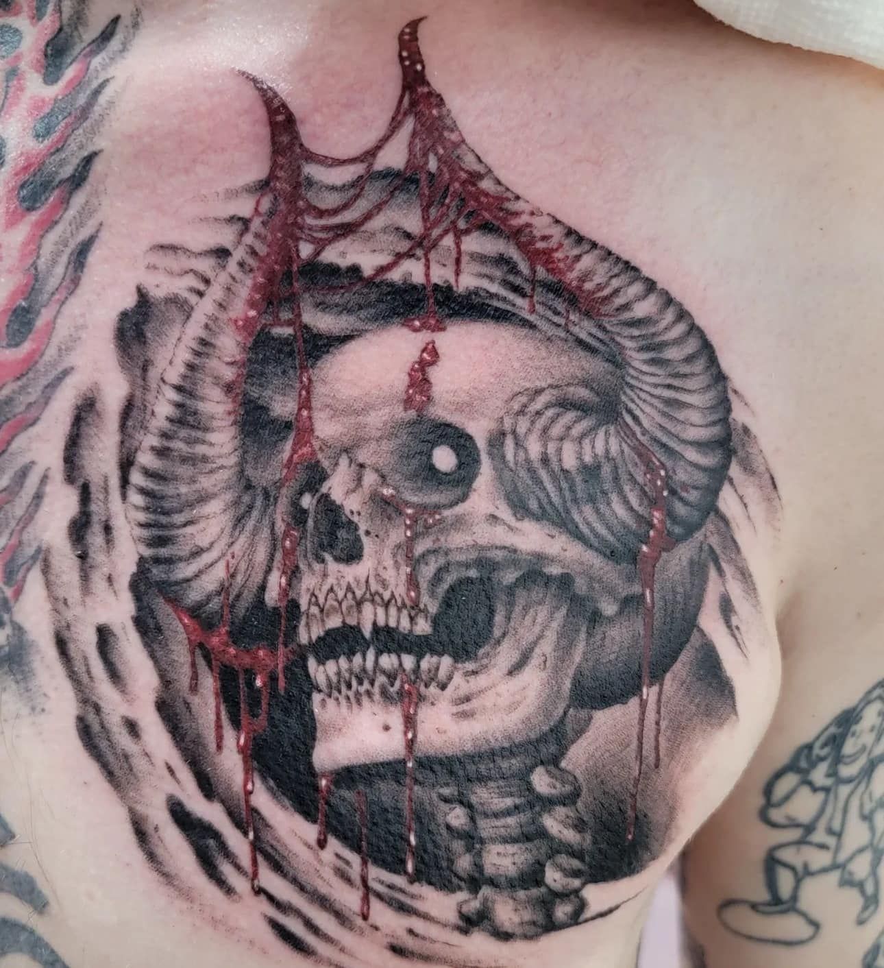 Black-and-gray skull tattoo with dripping details on upper back/shoulder skin