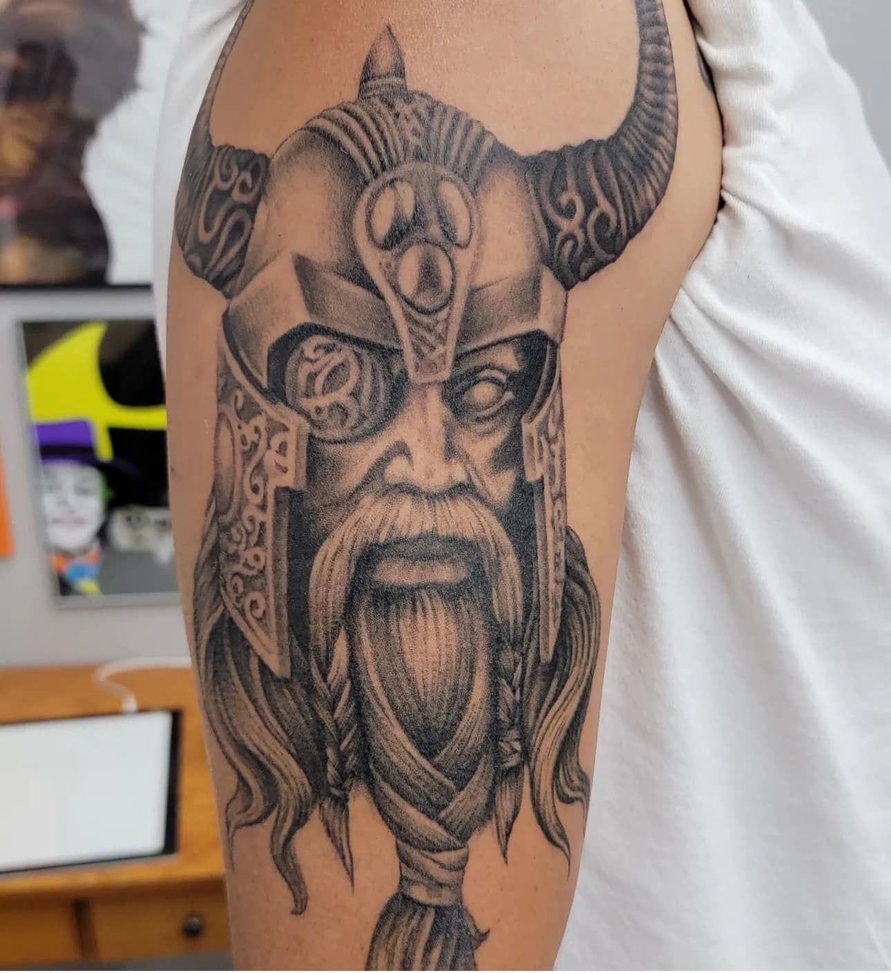 Black Viking-style face tattoo on a person’s upper arm with horned helmet and braided beard