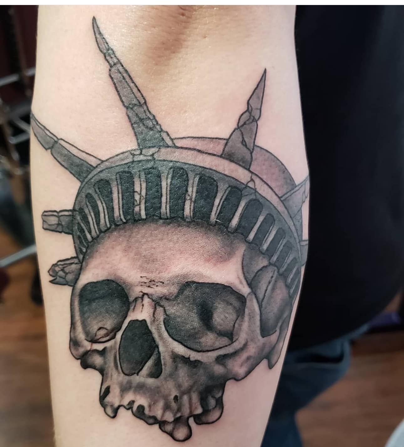 Black-and-gray skull tattoo with the Statue of Liberty crown on an arm
