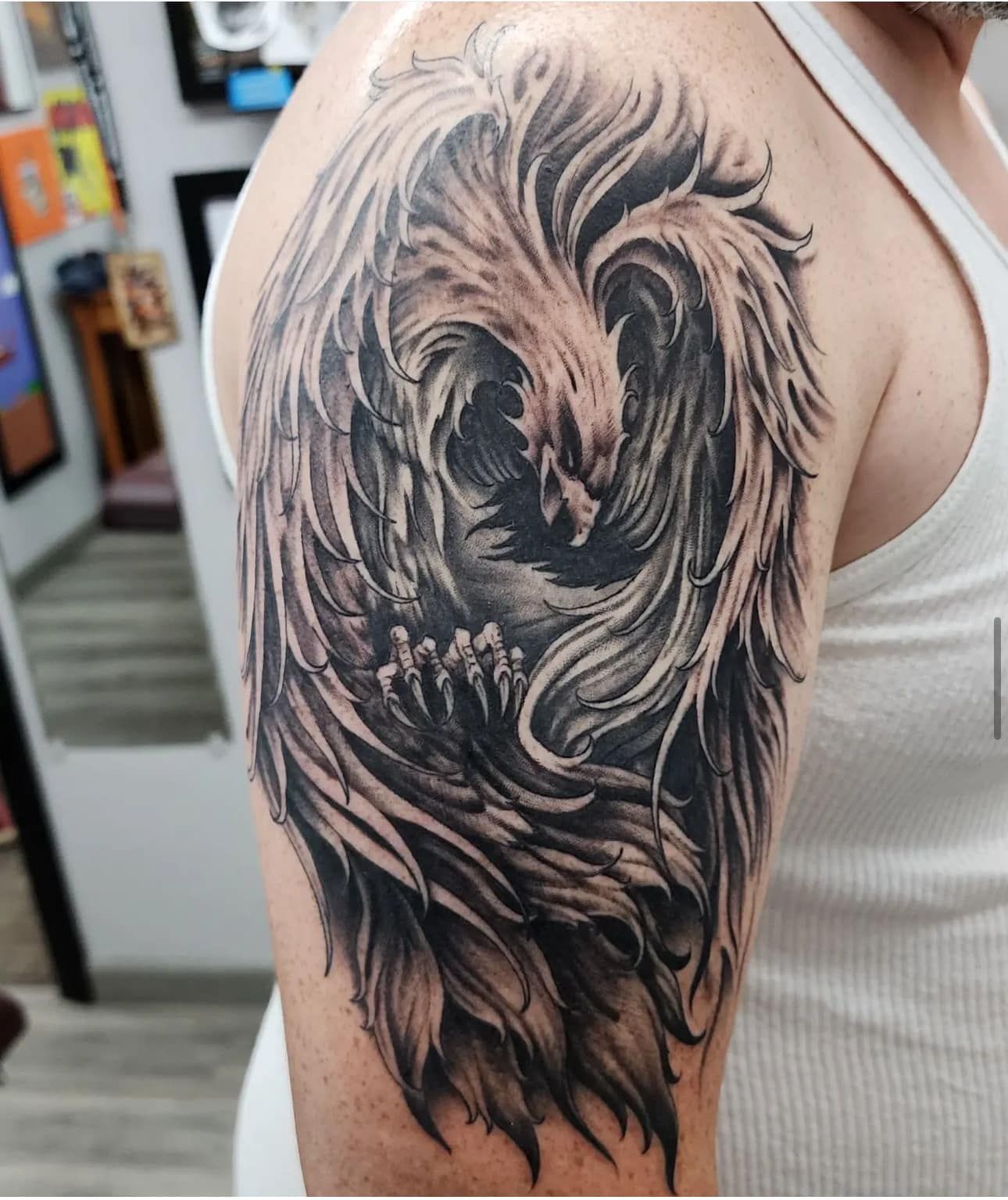 Close-up of a black-and-gray bird tattoo on an upper arm in a tattoo shop