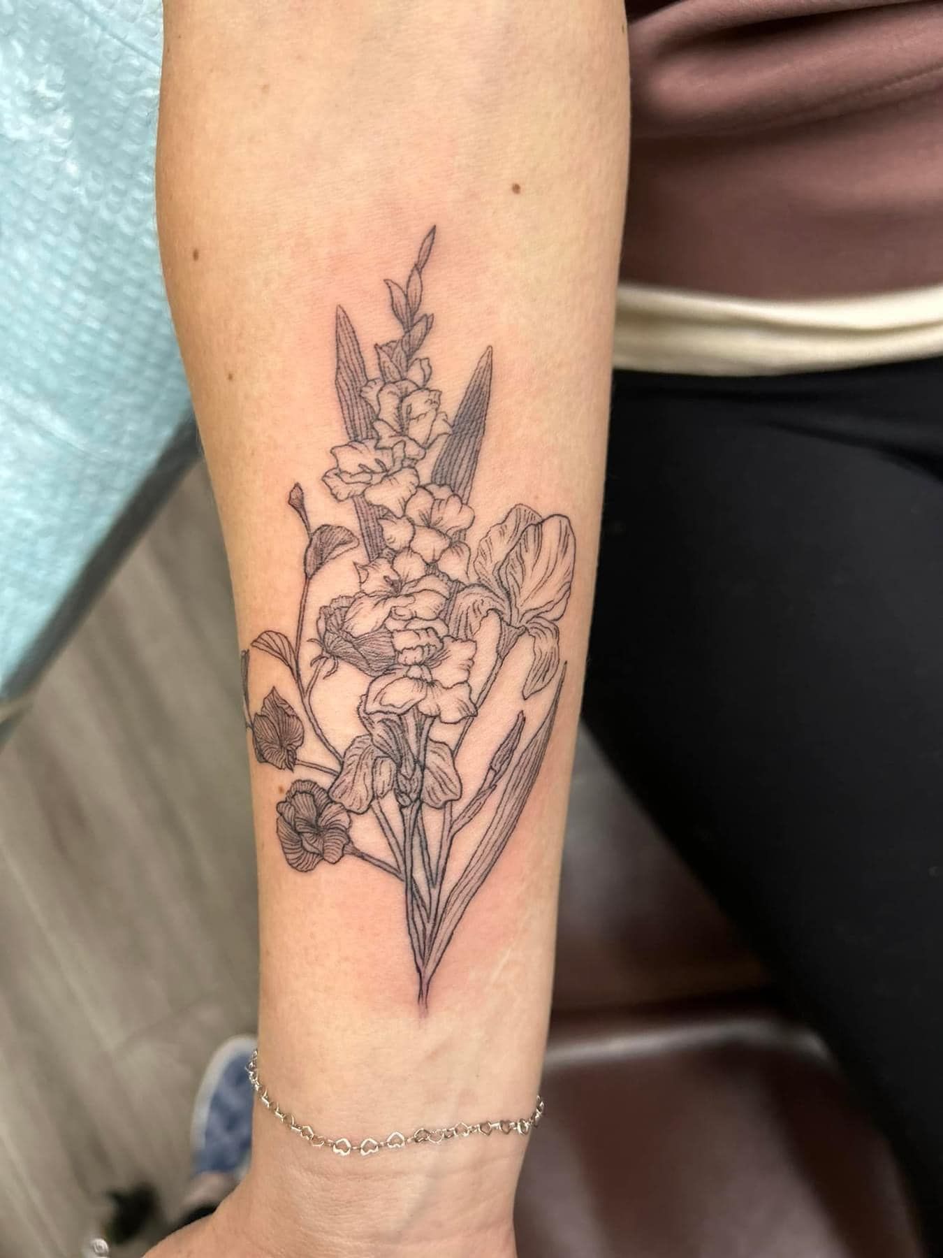 Floral line-art tattoo on a person’s forearm, with a thin bracelet near the wrist.