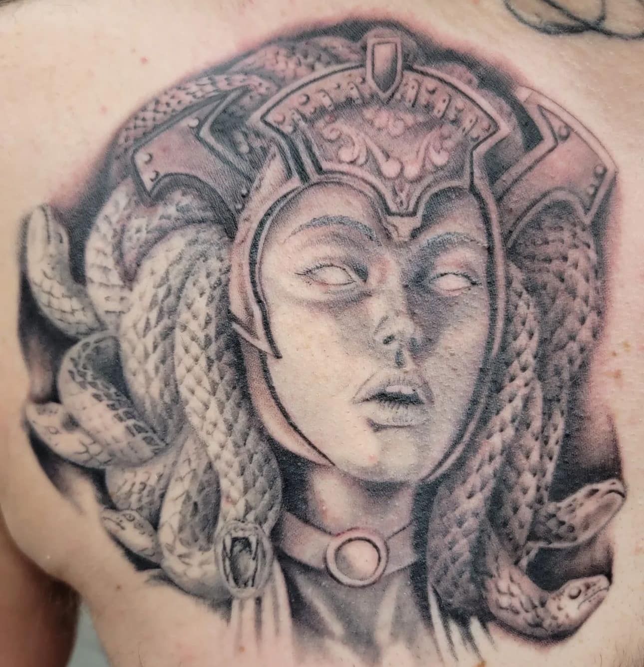 Black-and-gray tattoo of a Medusa-like face with braided snakes and ornate headpiece
