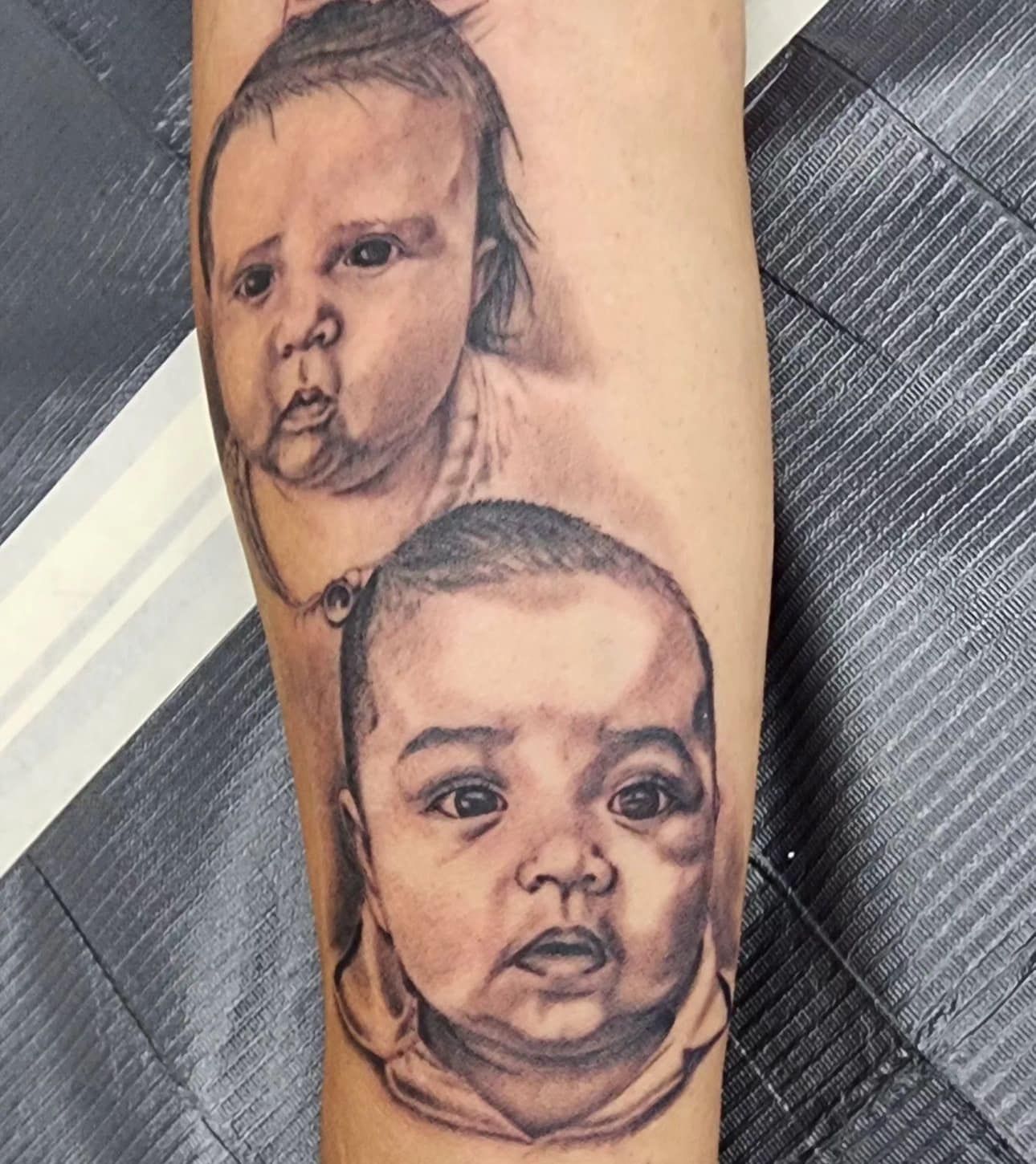 Two realistic black-and-gray baby face tattoos on a forearm