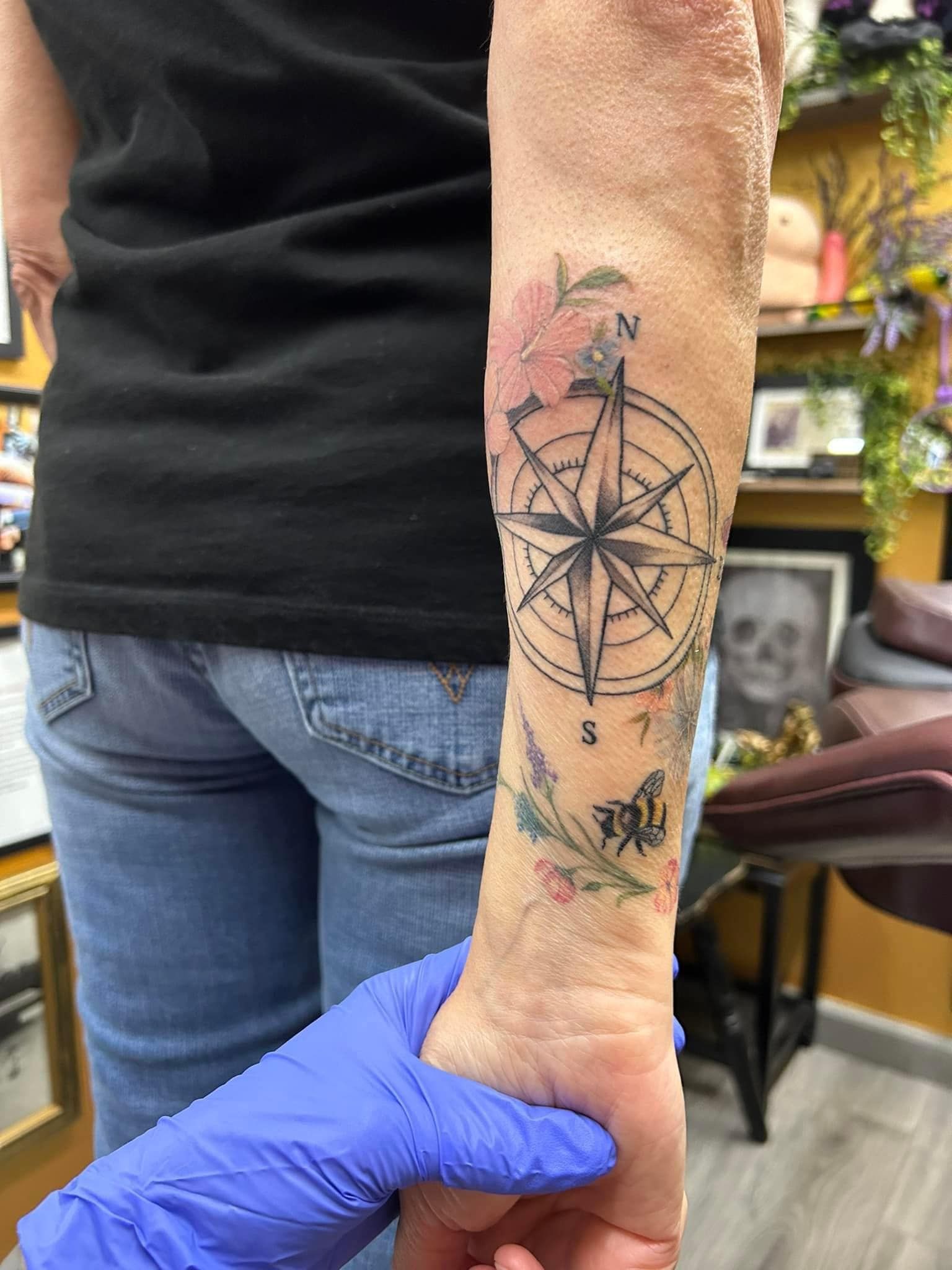 Arm tattoo with compass and floral design on a forearm being held by a gloved hand