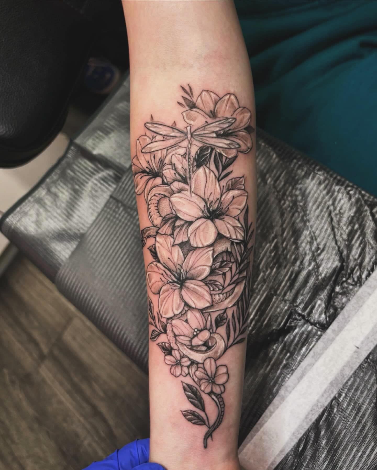 Black floral tattoo design on a forearm with detailed flowers and leaves.