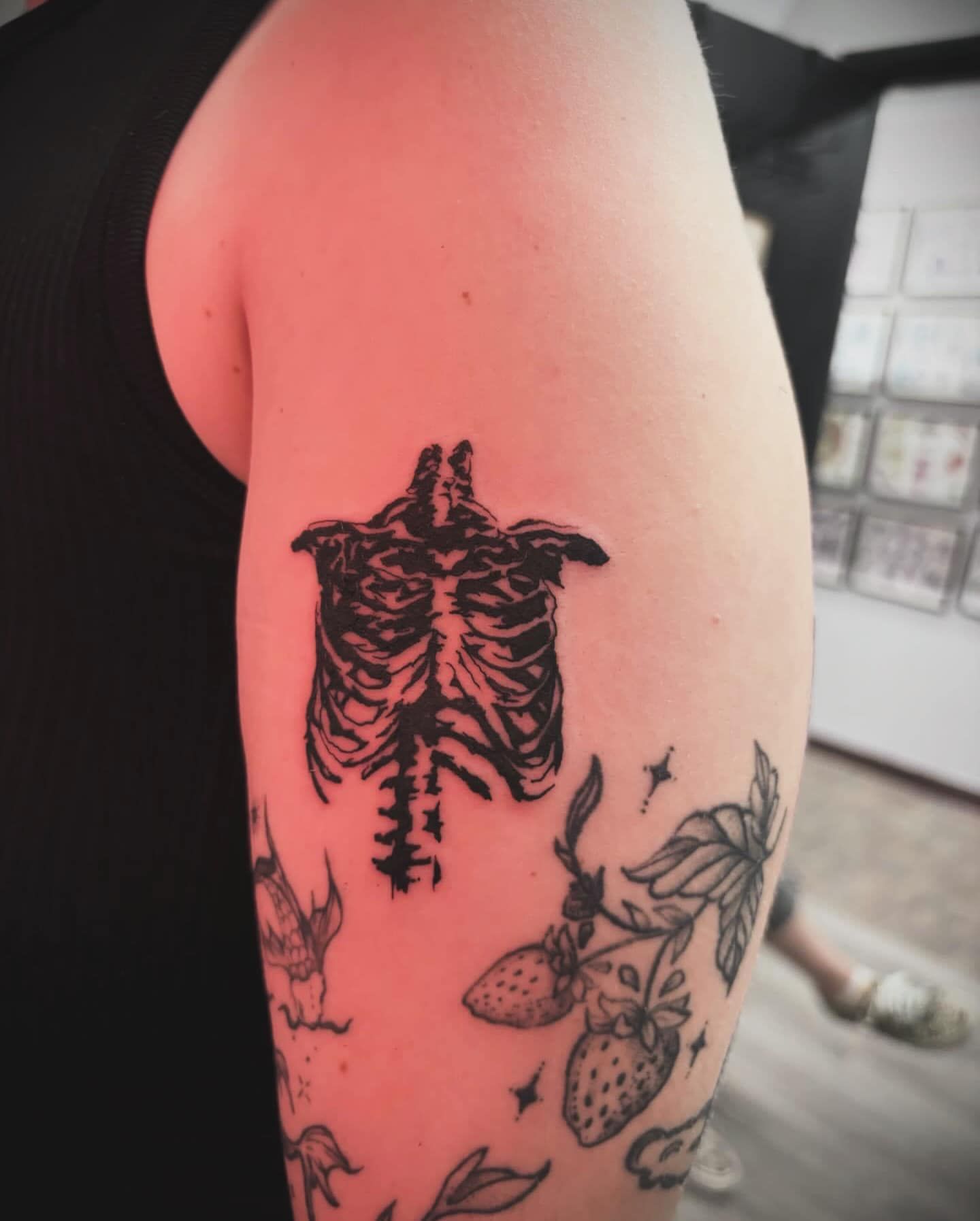 Close-up of an upper arm with a black skeleton tattoo and surrounding berry and star tattoos.