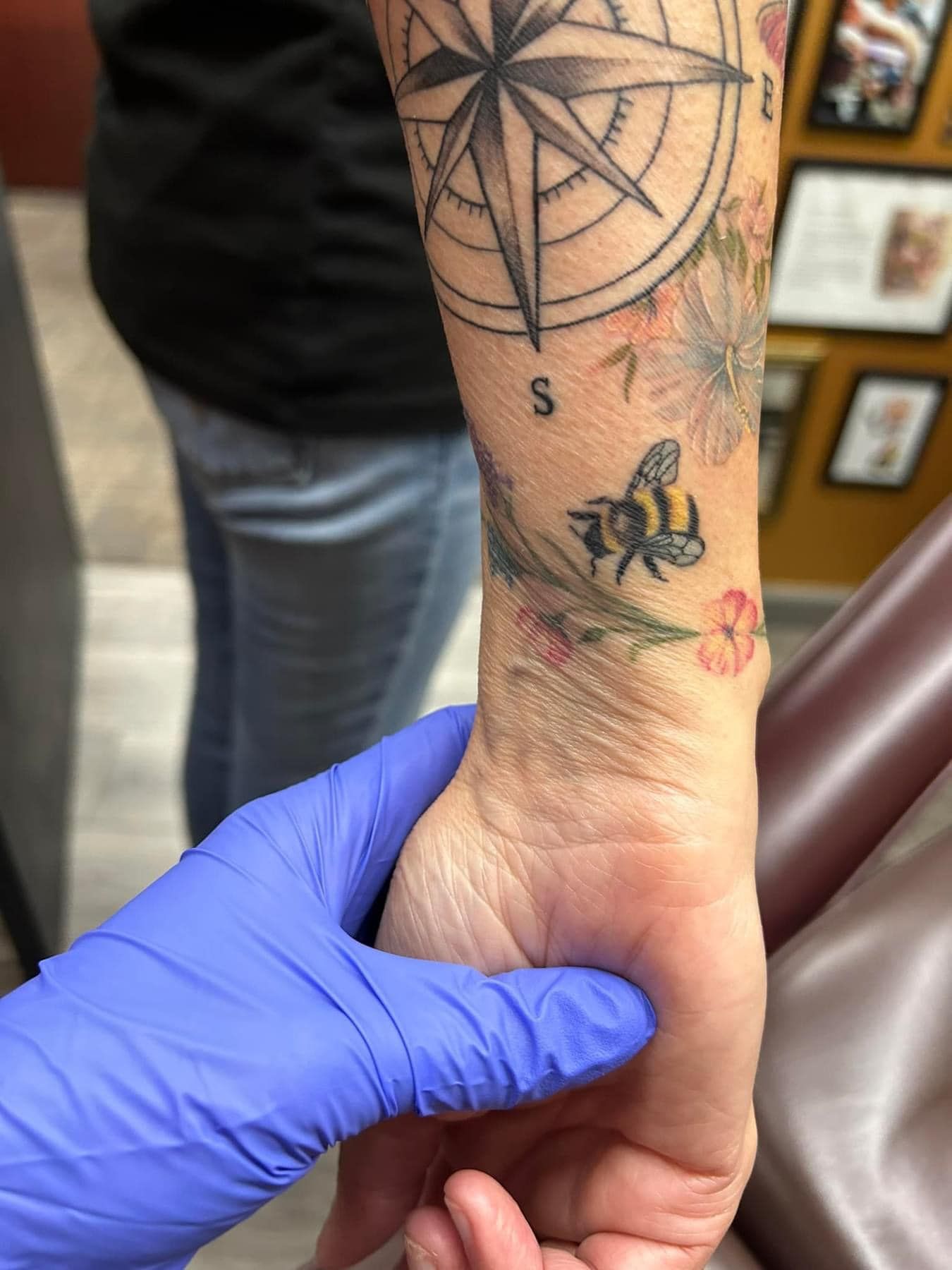 Gloved hand holding a tattooed wrist with a small red rash near the thumb in a clinical setting