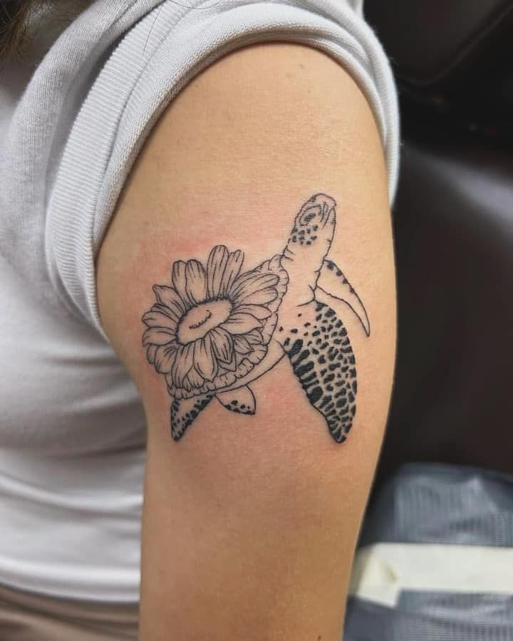 Tattoo of a turtle with a flower on a person's upper arm