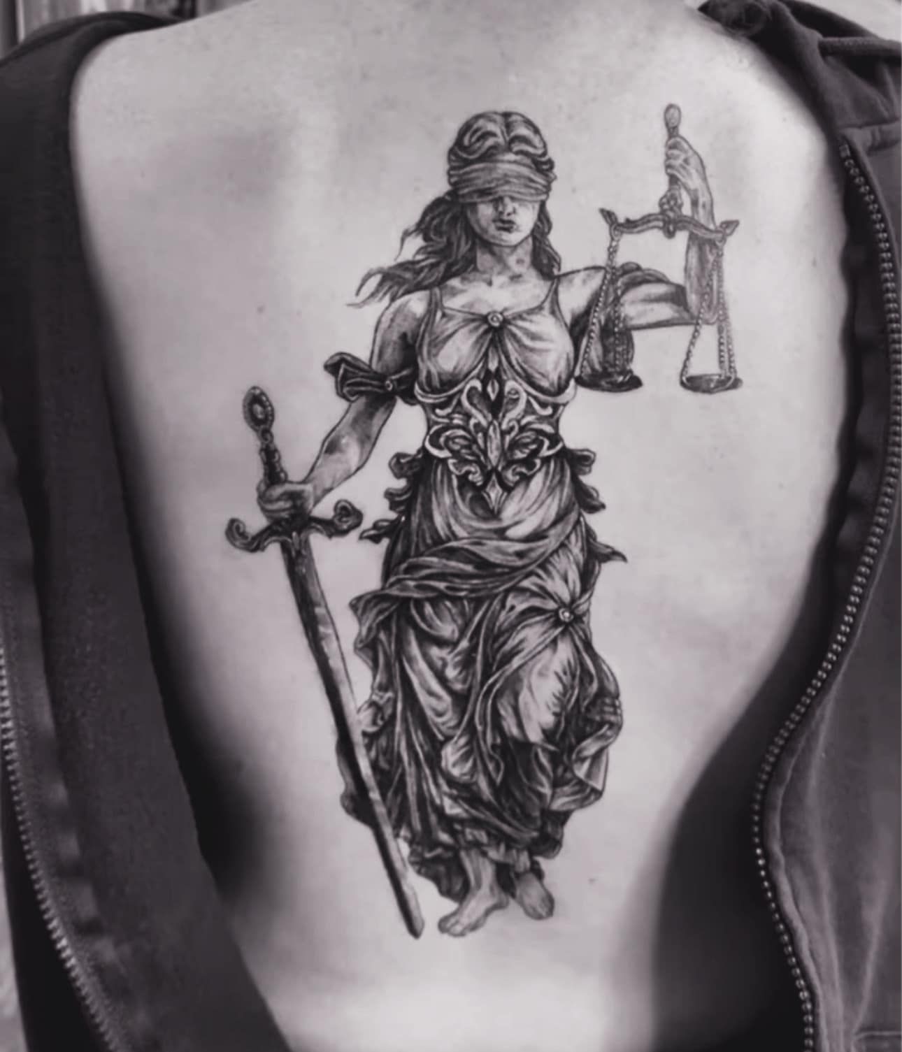 Black-and-gray tattoo of Lady Justice holding scales and a sword on a person's back