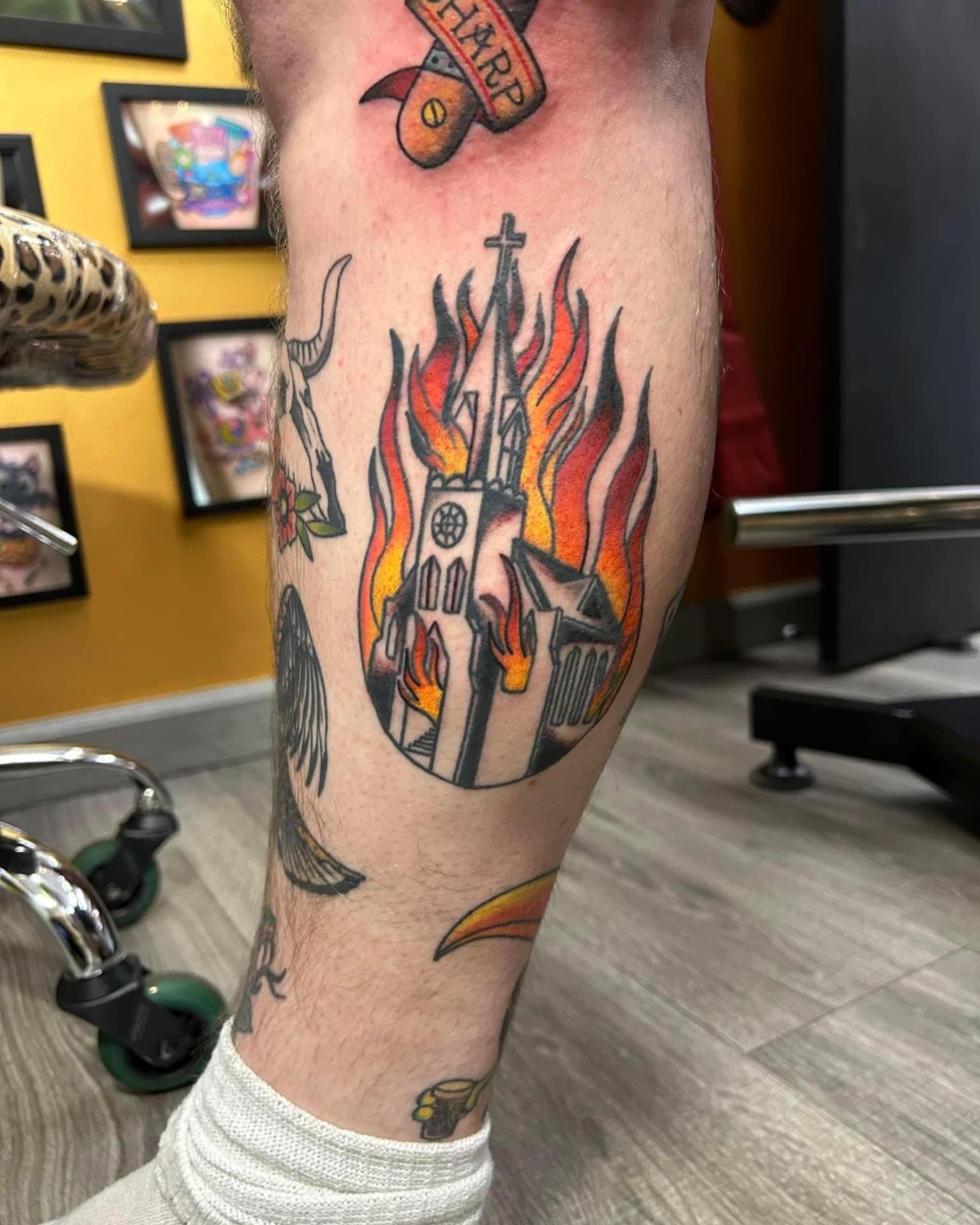 Close-up of a tattooed lower leg with a colorful burning building tattoo in a studio setting