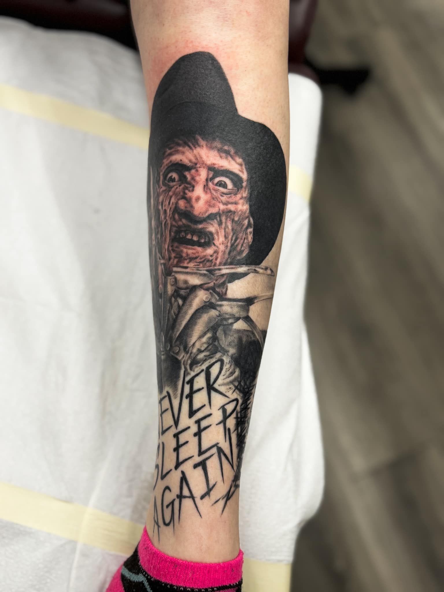 Forearm tattoo of a man’s face in a black hood with the words “NEVER FEEL GUILTY” below