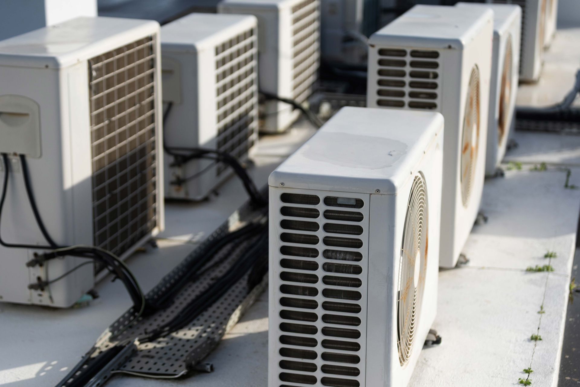 Outdoor row of white HVAC units with black vents and cables on a rooftop under sunlight