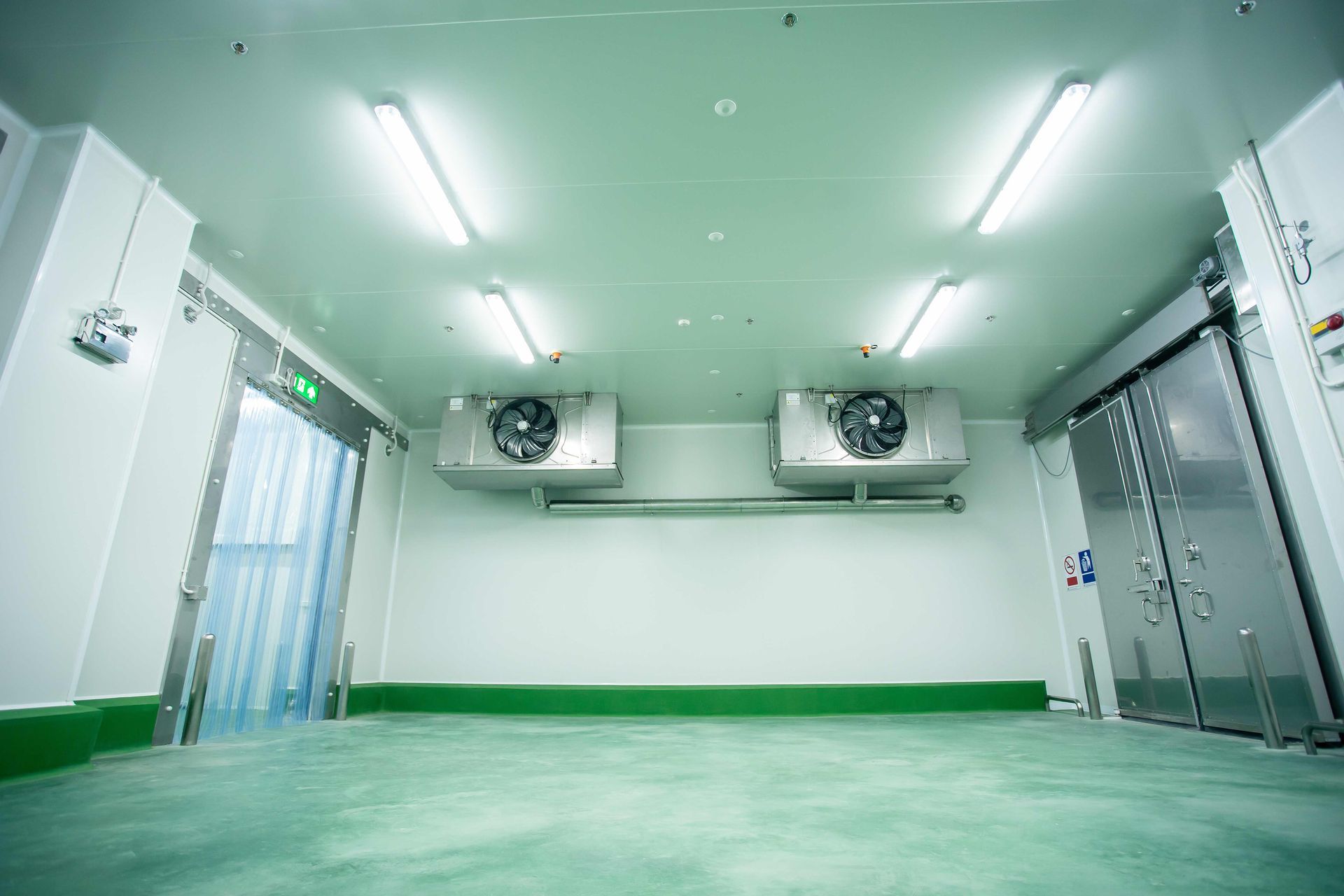 Empty clean industrial room with green floor, white walls, ceiling lights, and large ventilation units