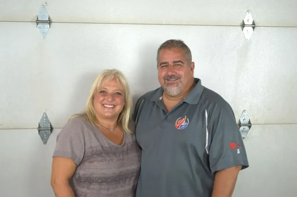 Two people smiling and standing together in front of a white garage door.