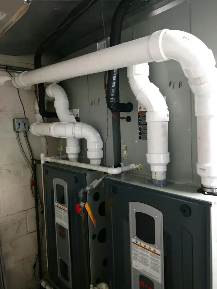 Industrial utility room with two gray HVAC units and white PVC pipes overhead