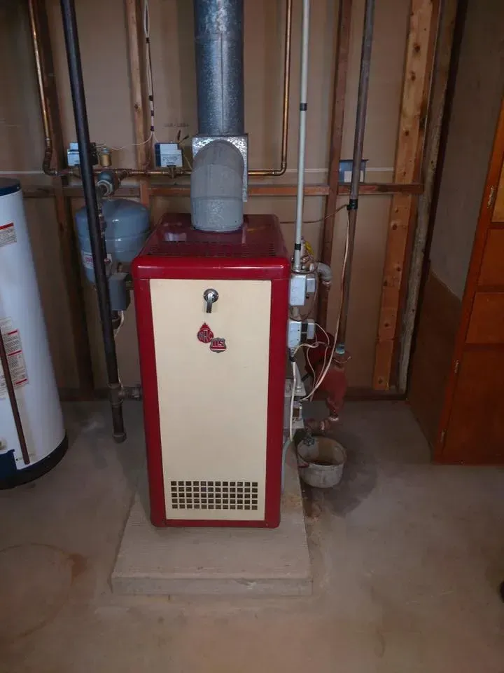 Red furnace with beige front panel and metal vent pipes in a basement utility room