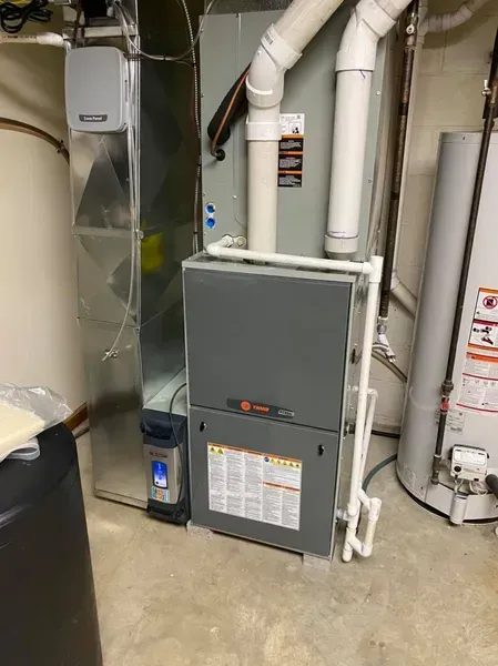 Gray furnace and HVAC ducts in a utility room next to a water heater.
