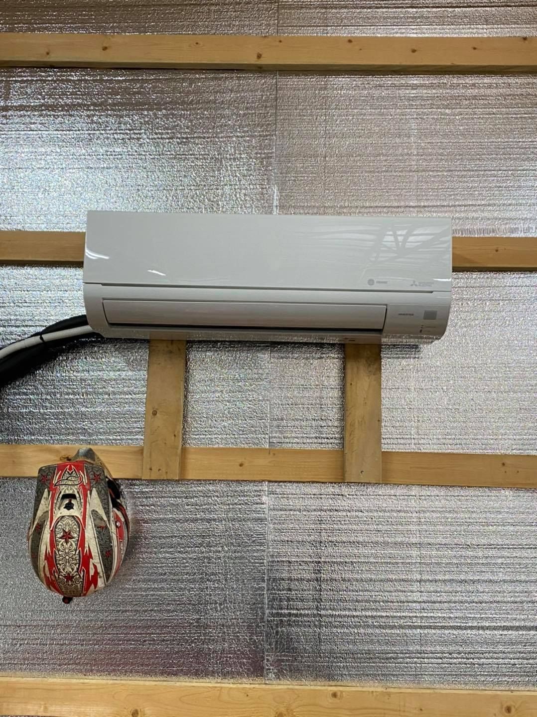 Wall-mounted white air conditioner above a decorative hanging ornament on a slatted wall.