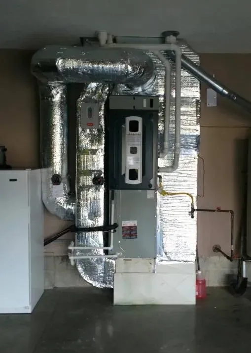 Large HVAC/furnace unit with silver ductwork and pipes in a utility room