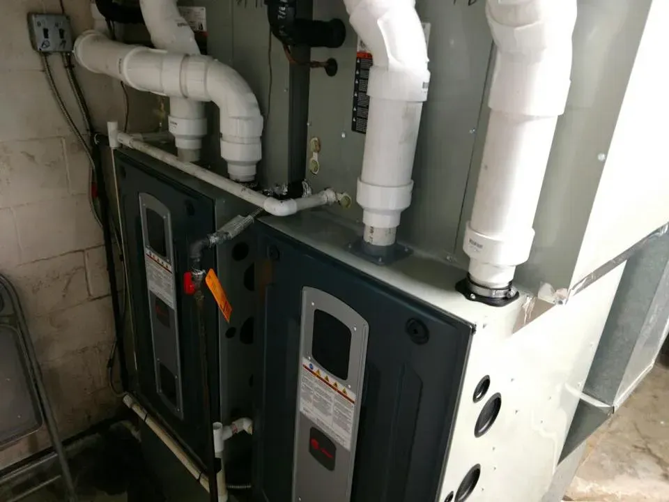 Row of gray HVAC units with white insulated pipes in a utility room