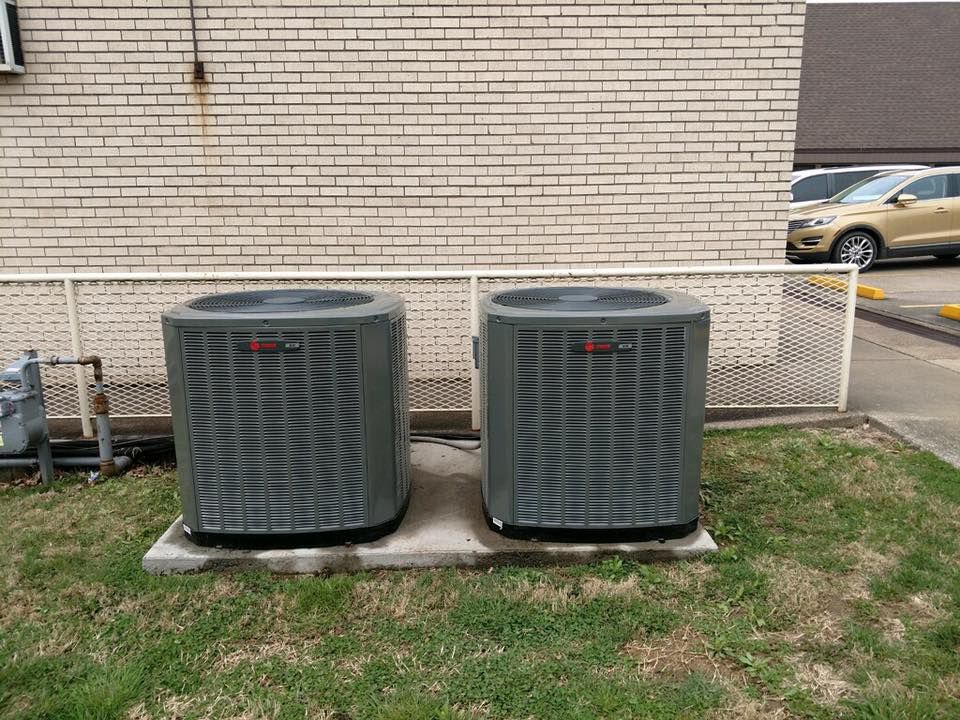 HVAC technician beside outdoor air conditioner and furnace boxes in a driveway