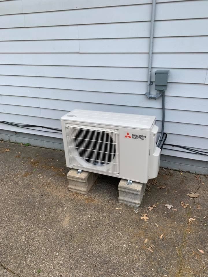 Outdoor Mitsubishi mini-split AC unit beside a white house wall on concrete blocks