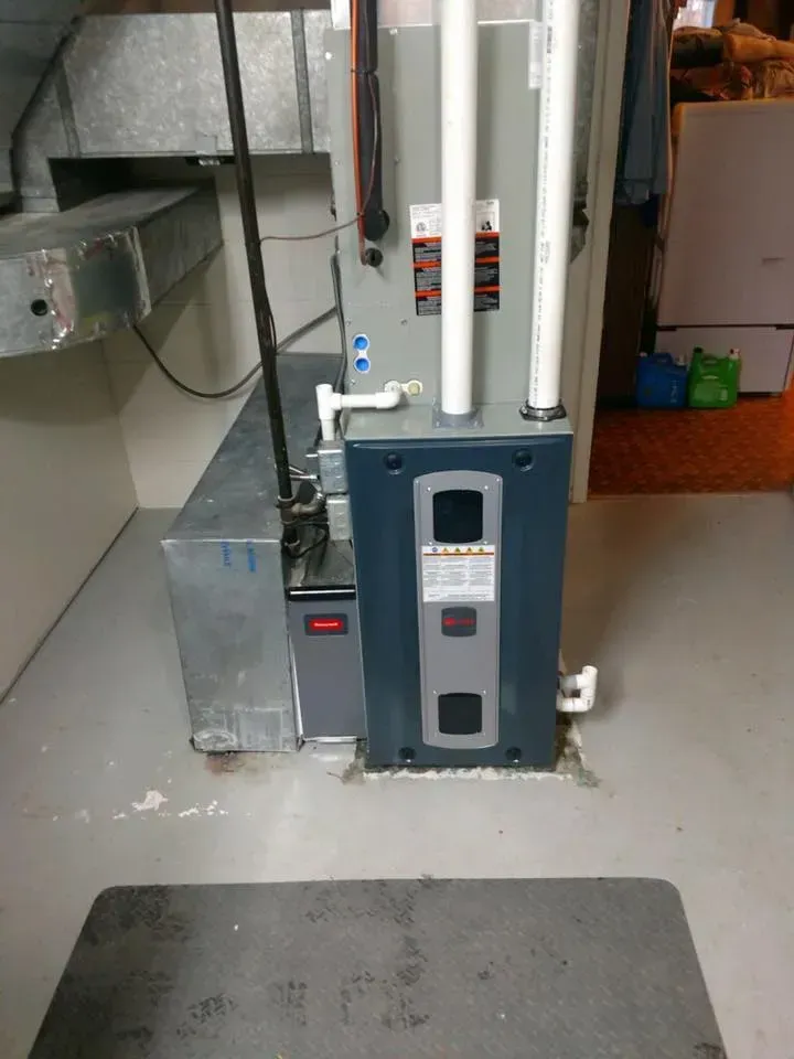 Basement utility room with a gray water heater or boiler and exposed pipes on a concrete floor