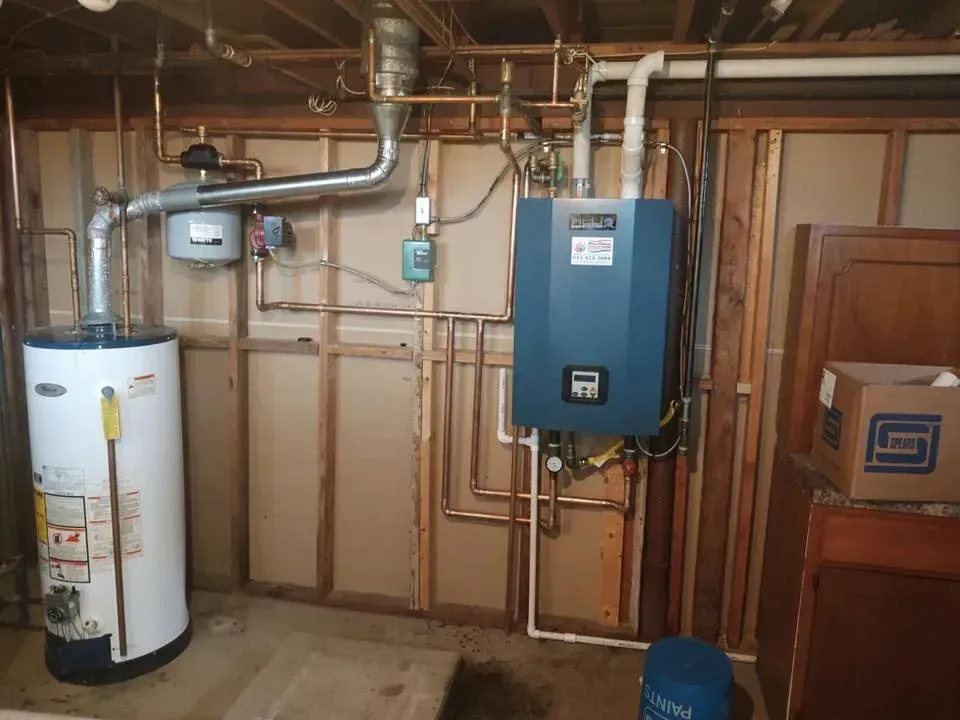 Basement utility room with water heater, blue boiler, pipes, and electrical panel against unfinished walls