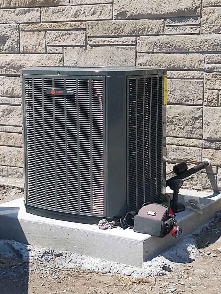 Outdoor HVAC unit beside a stone wall, connected to an air compressor on a concrete pad