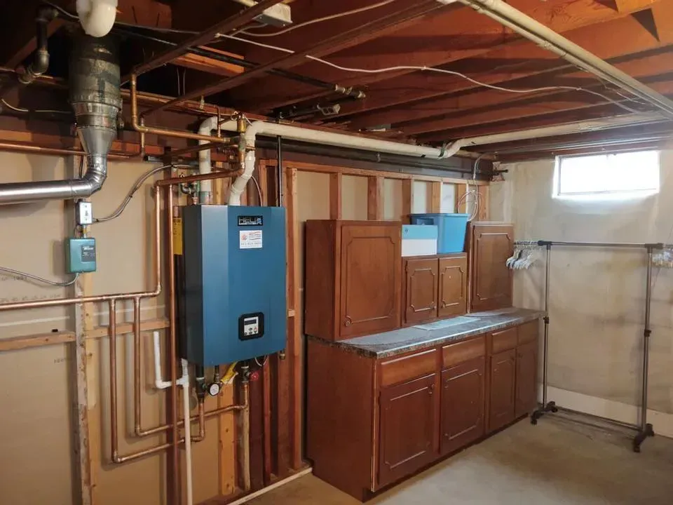 Basement laundry area with water heater, blue utility panel, and brown cabinets along a concrete wall.