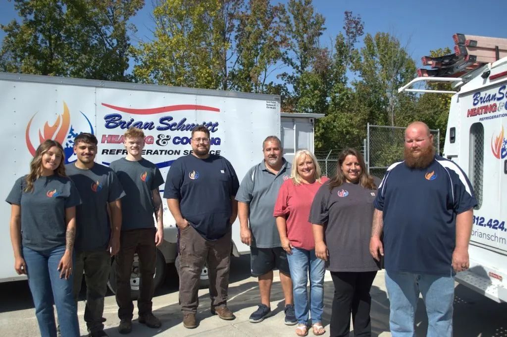 Group of employees posing outdoors beside a Brinks Security service truck and trailer under sunny skies