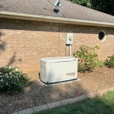 Generac standby generator beside a brick house with a utility meter and shrubs in the yard