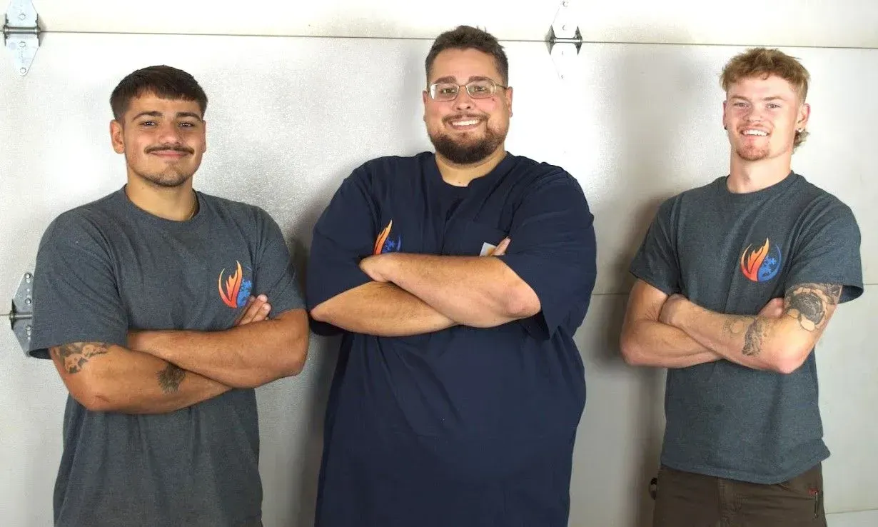 Three men stand with arms crossed against a light wall, wearing dark shirts and smiling.