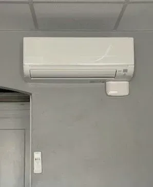 Wall-mounted white air conditioner above a gray wall with a small remote below.