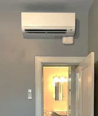 Wall-mounted white air conditioner above an open door in a gray room