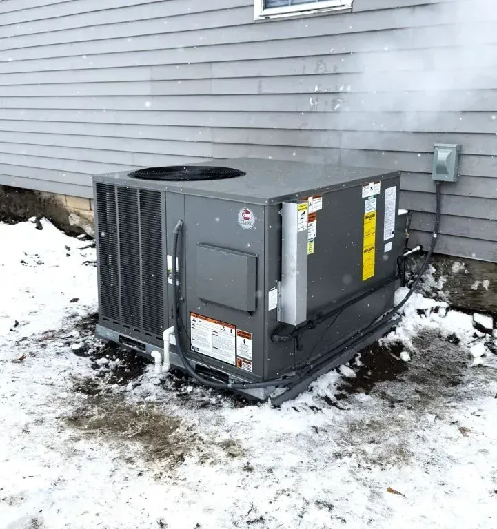 Outdoor HVAC unit beside a house wall on snow-covered ground