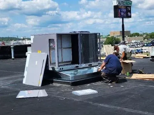 Worker repairing rooftop HVAC unit on a flat roof under a cloudy sky