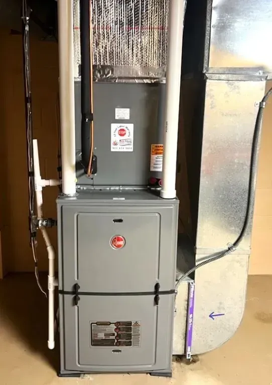 Residential furnace and ductwork in a utility closet, with gray metal panels and exposed silver ducts.