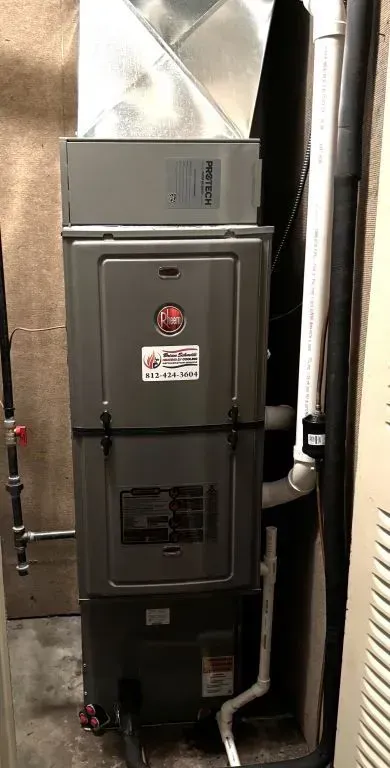 Gray HVAC unit in a narrow utility closet with ductwork and pipes, viewed from the front.
