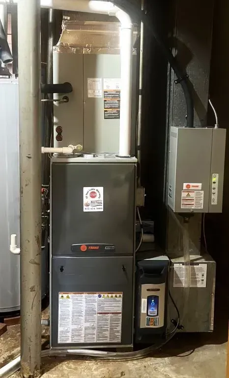 Indoor HVAC furnace unit with ductwork, pipes, and electrical panel in a utility closet