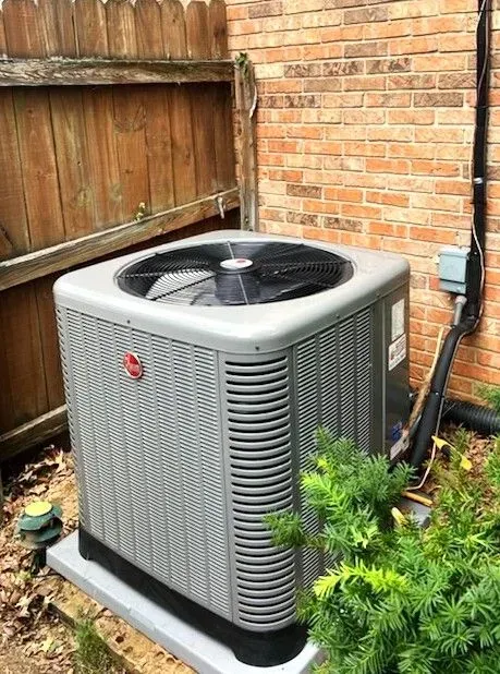 Outdoor air conditioner unit beside a wooden fence and brick wall in a backyard