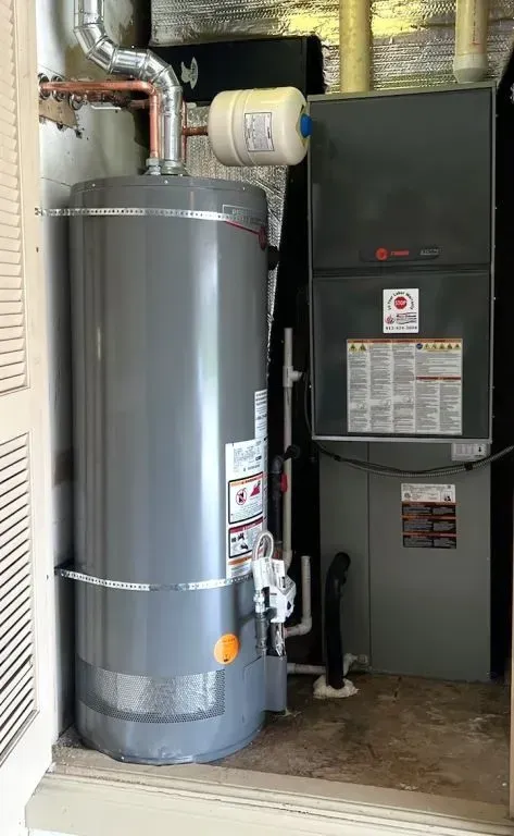 Water heater and HVAC furnace in a utility closet with exposed ductwork and piping.